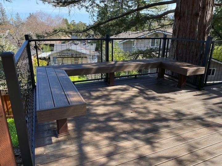 Deck with built-in bench seating under trees by DG Landscape Design