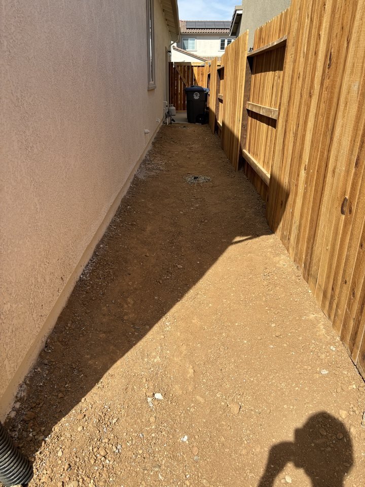 Narrow dirt side yard between the house and fence